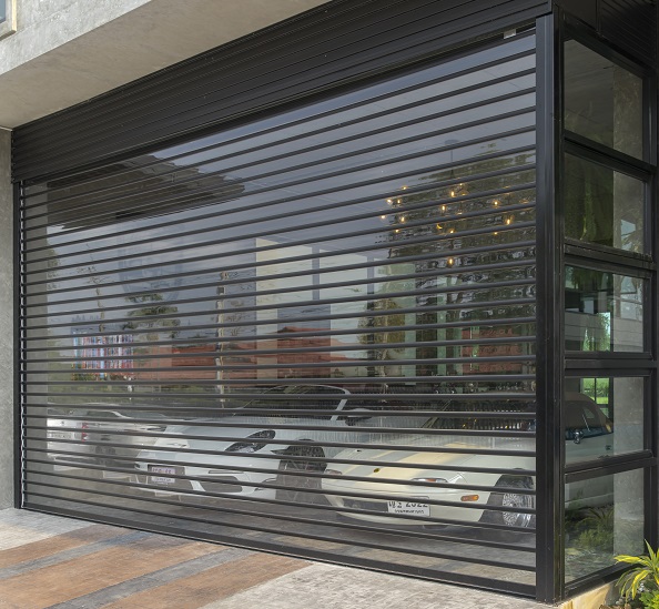 เลือกใช้ประตูแบบ shutter door เเผ่นใสโพลีคาร์บอเนต ที่มีความแข็งแรงทนทานต่อแรงกระแทกได้ดี มีน้ำหนักเบา ควบคุมการเปิด-ปิดด้วยรีโมท พร้อมระบบเซฟตี้เซ็นเซอร์