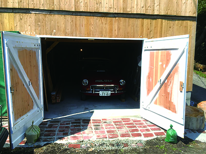 ทำหลังคา ติดแผ่นผนัง เมื่อฝ่าฟันเรื่องของฝนไปได้ก็รู้สึกผ่อนคลาย แล้วหยุดมากกว่าครึ่งปีก่อนที่จะเริ่มทำประตู แนวนอนและแนวตั้งของด้านหน้าประตูไม่ได้สมบูรณ์แบบ ดังนั้น ประตูทั้ง 4 บานจะต้องจัดรูปแบบอีกที ทำขนาดใหญ่ไว้ก่อนแล้วค่อยตัดออกให้เหมาะสม บานพับประตู ไม่เจอแบบที่ชอบจึงสั่งนำเข้าแบบที่ใช้กับโรงนาของประเทศอังกฤษ หน้าต่างสี่เหลี่ยมเล็กๆ ที่ประตูใช้แบบมีกรอบโดยซื้อที่ร้าน 100 เยน ประตูทำขนาดมาตรฐานและสูงประมาณส่วนสูงของผม ความกว้าง ด้านขวาสำหรับ MGB ด้านซ้ายสำหรับ MG Midget ที่แคบกว่า ประตูด้านซ้ายสุดมีทางเดินด้วยจึงแคบ