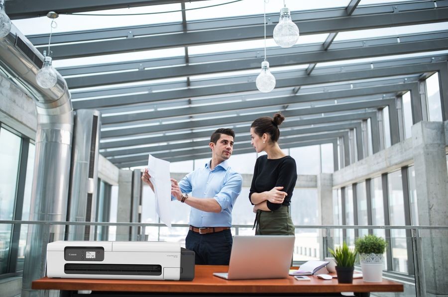 Two young architects with blueprints and model of a house standing in office, talking.